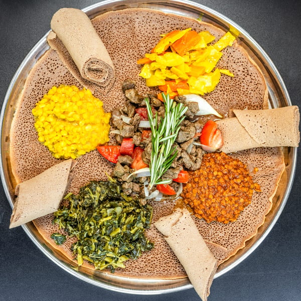 Ethiopian injera platter with various stews, vegetables, and meat, garnished with rosemary.