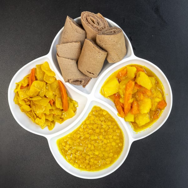 Ethiopian injera bread with three vegetable dishes: yellow lentils, cabbage, and potatoes with carrots.