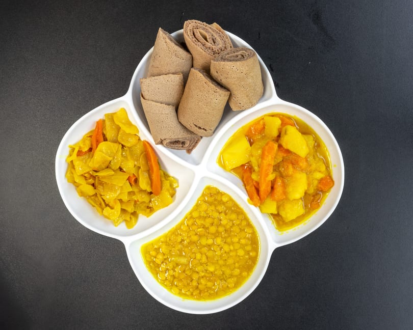 Ethiopian injera bread with three vegetable dishes: yellow lentils, cabbage, and potatoes with carrots.