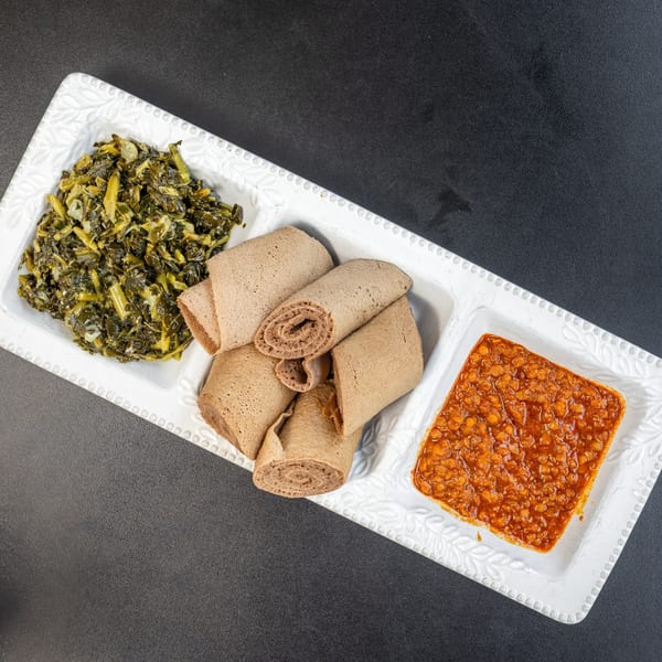 A white rectangular plate with three sections, holding green collard greens, rolled injera bread, and red lentils.
