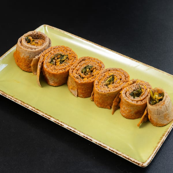 Six injera rolls filled with orange lentils and green vegetables, arranged on a light green rectangular plate.