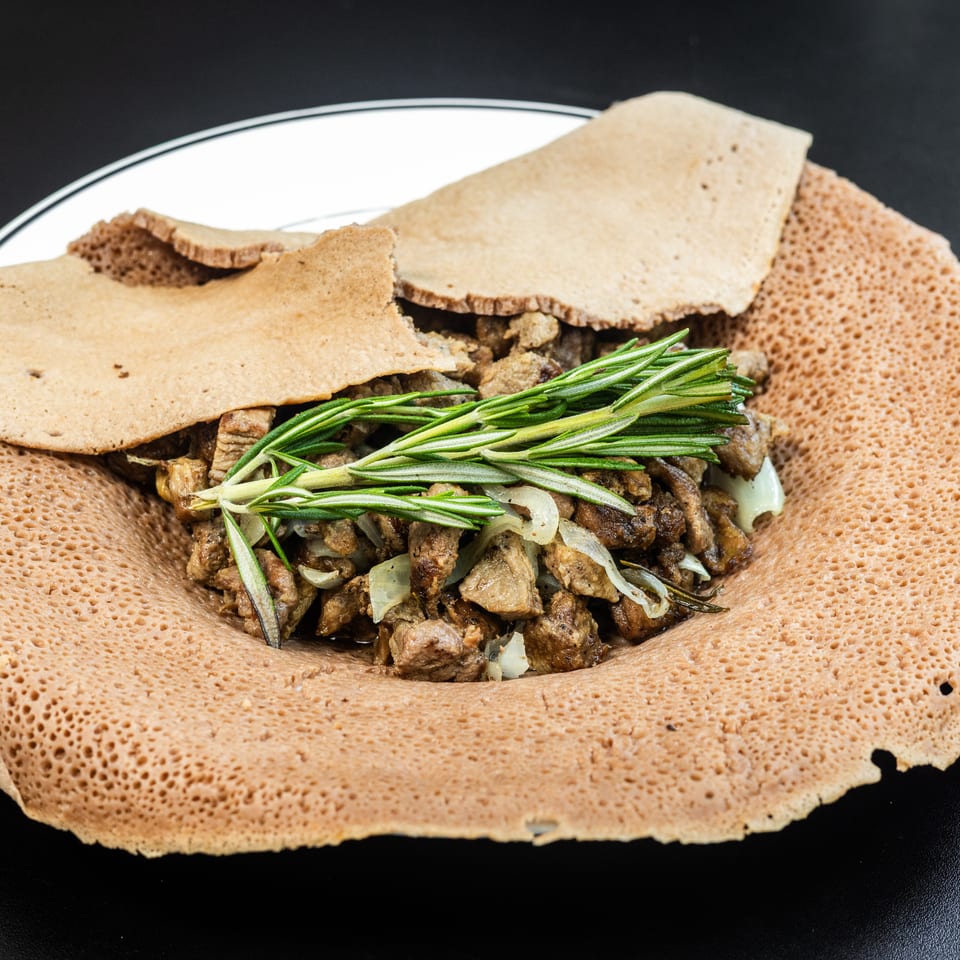 Ethiopian injera bread with meat, onions, and rosemary on a white plate.