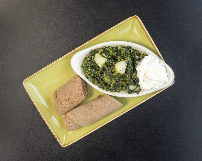 Ethiopian Gomen with potatoes and cheese, served with injera bread on a green rectangular plate.