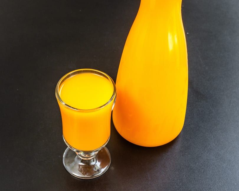 A glass and a bottle filled with vibrant orange juice, set against a dark background.