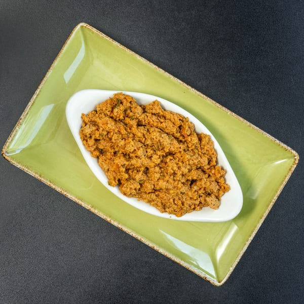 A white oval dish filled with a savory, textured orange-brown meat mixture, on a green rectangular plate.
