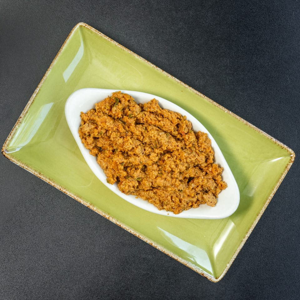 A white oval dish filled with a savory, textured orange-brown meat mixture, on a green rectangular plate.