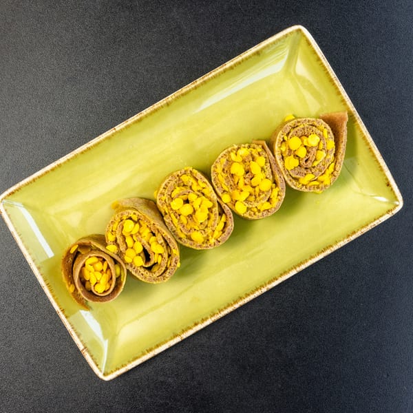 Five corn-filled crepes, rolled and sliced, arranged on a rectangular green plate.