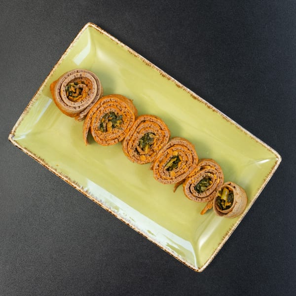Savory crepes filled with orange spread and green vegetables, arranged on a light green rectangular plate.