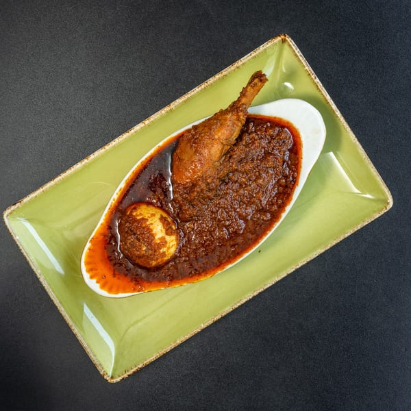 Chicken drumstick and a hard-boiled egg in a rich, dark red sauce, served on a green plate.