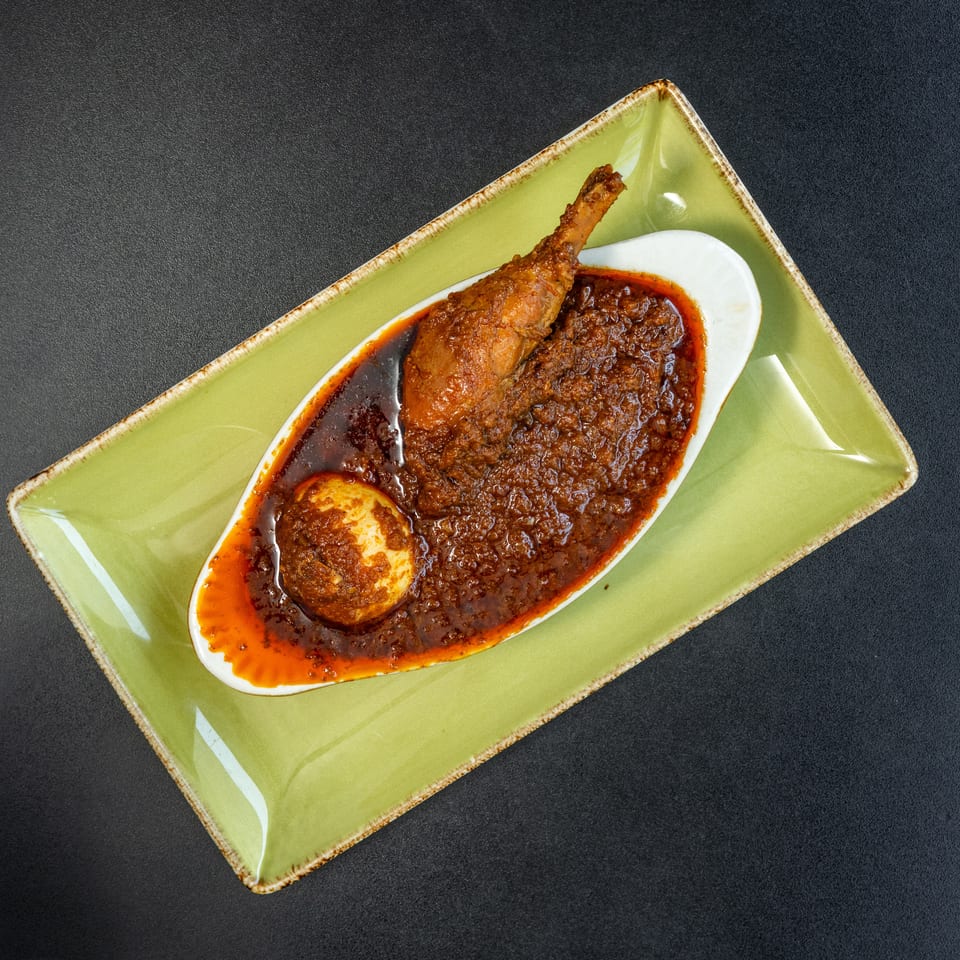 Chicken drumstick and a hard-boiled egg in a rich, dark red sauce, served on a green plate.