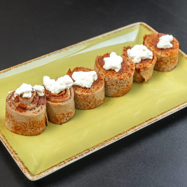 Five rolled crepes with a red filling and white cream topping, on a light green rectangular plate.