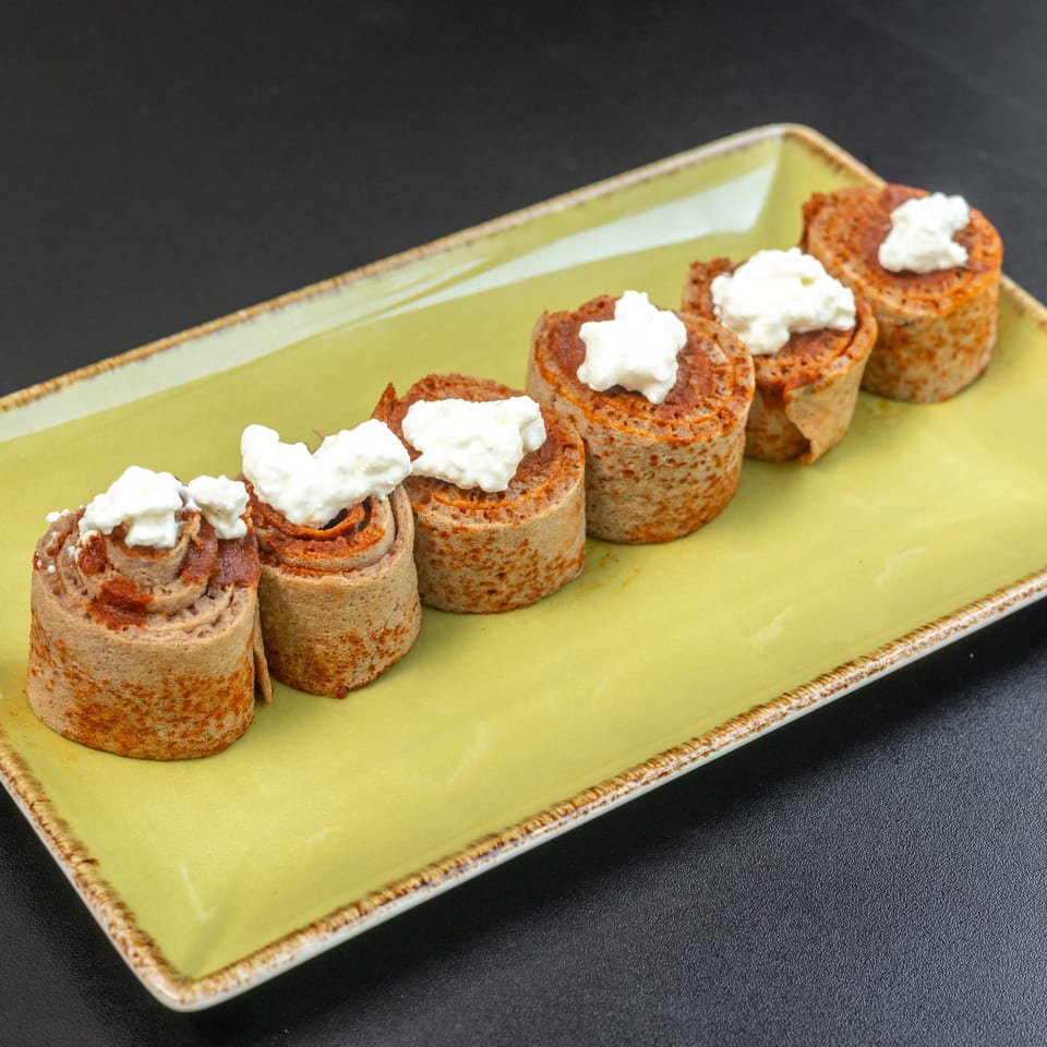 Five rolled crepes with a red filling and white cream topping, on a light green rectangular plate.