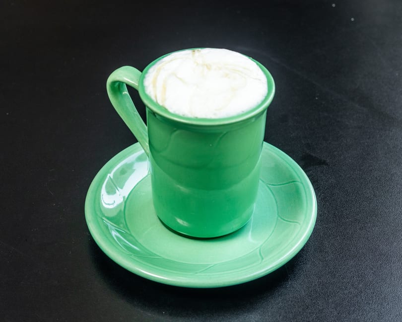 A bright green mug filled with a frothy white drink, served on a matching saucer.