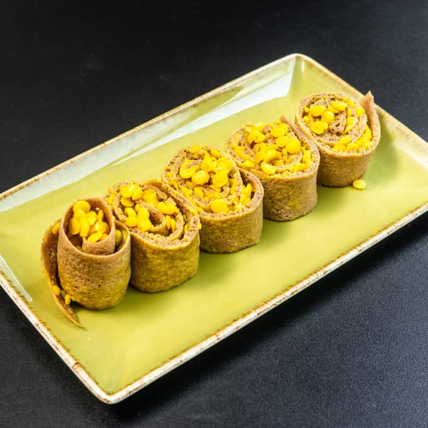 Five corn-filled crepes, rolled and arranged on a rectangular green plate against a dark background.
