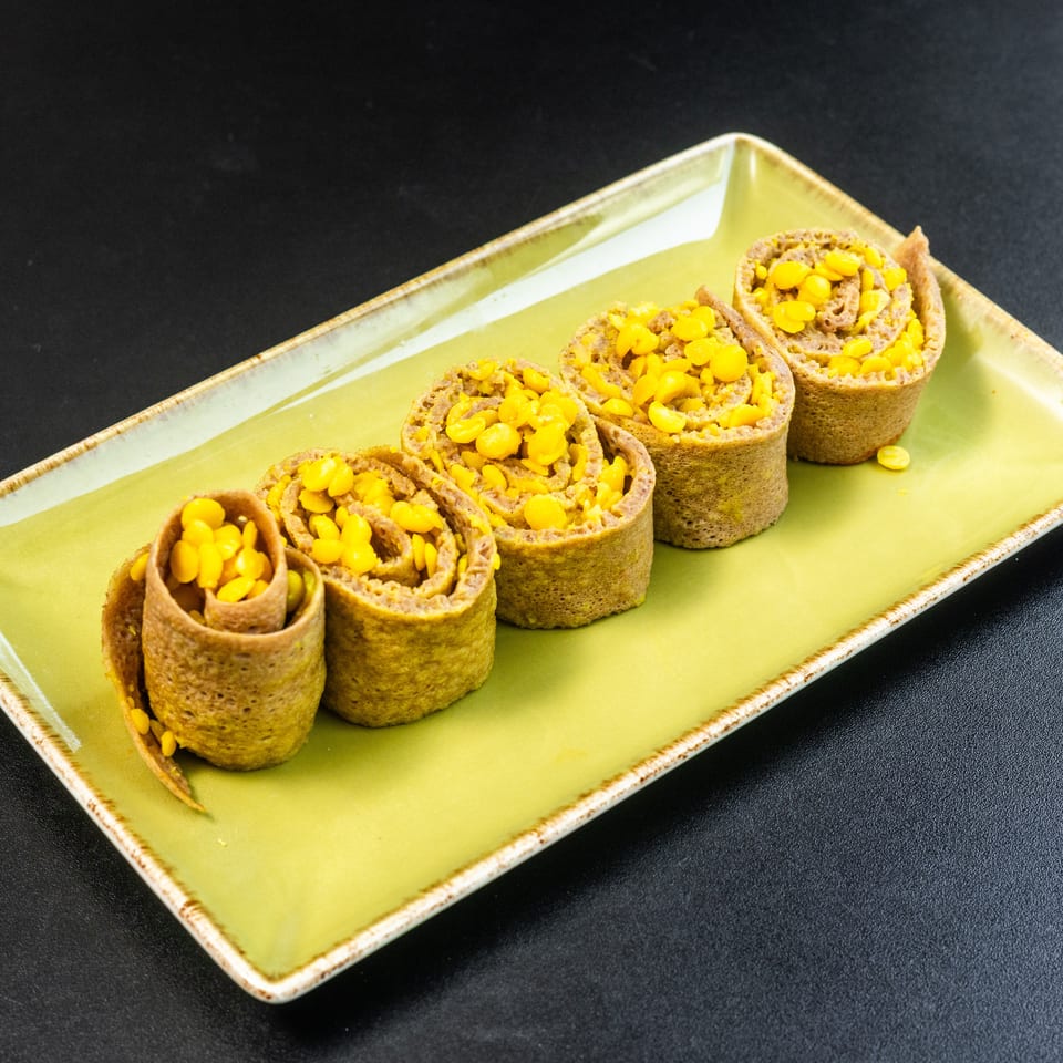 Five corn-filled crepes, rolled and arranged on a rectangular green plate against a dark background.