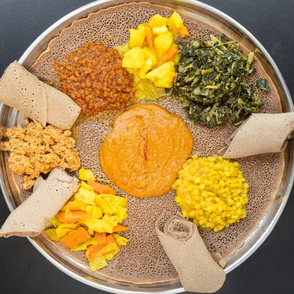 Overhead view of a large platter of Ethiopian food with injera bread and various colorful stews.
