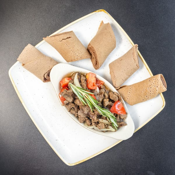 Ethiopian tibs, a meat dish with tomatoes, onions, and rosemary, served with injera bread.