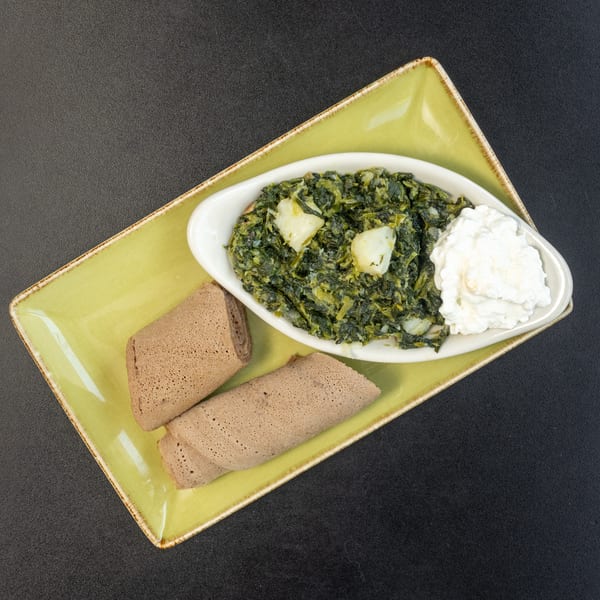 Ethiopian Gomen, collard greens with potatoes and cheese, served with injera on a green plate.